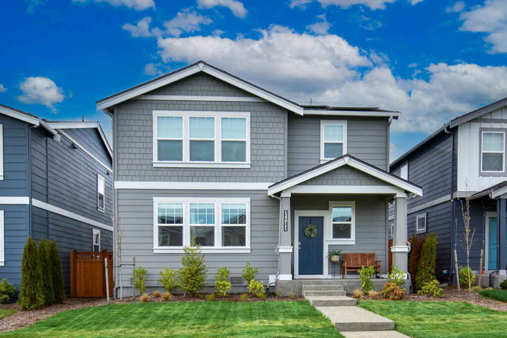 Photo of Grey House, white trim and a Navy front door with a blue cloudy sky. 